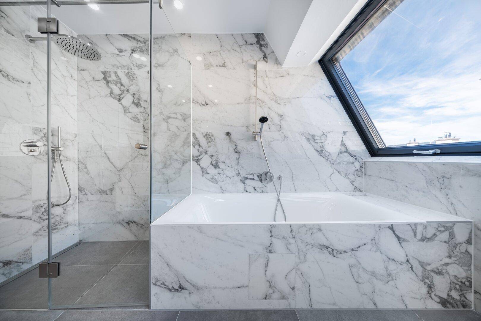 Elegantes Badezimmer mit Marmorverkleidung, Badewanne und begehbarer Dusche unter einem Dachfenster.