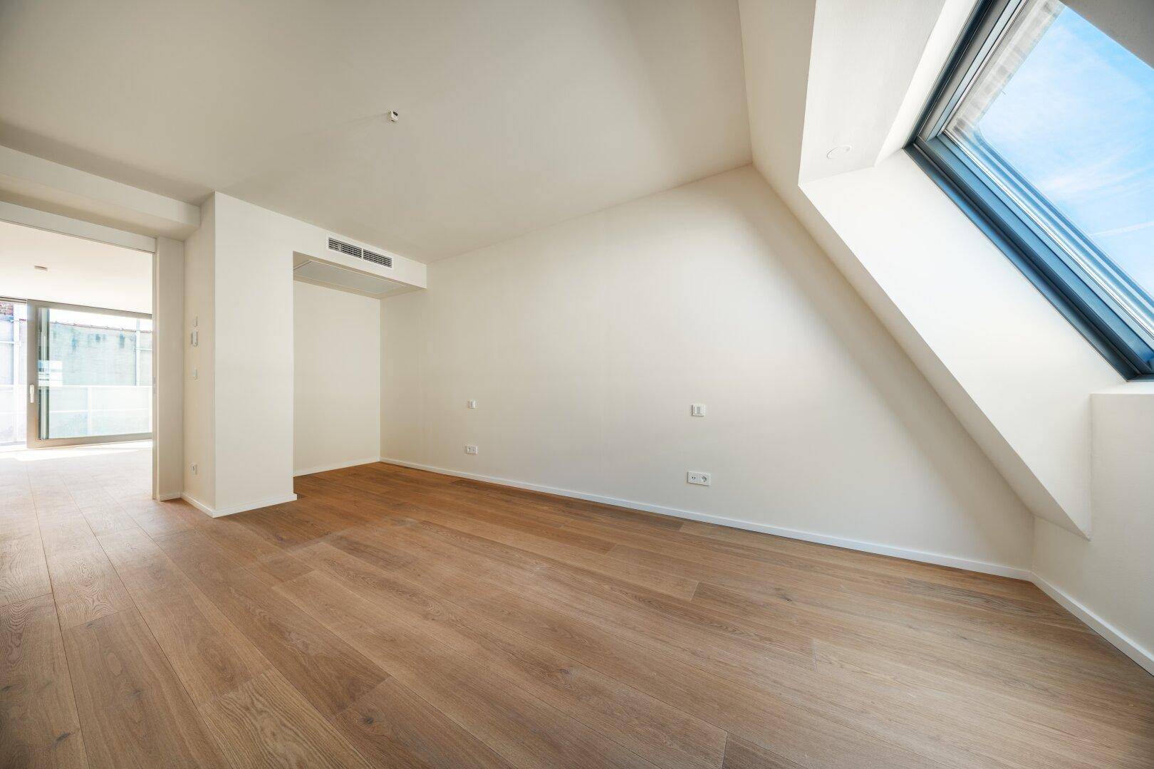 Helles Zimmer im Dachgeschoss mit Holzboden und großem Dachfenster, ideal als Schlafzimmer.