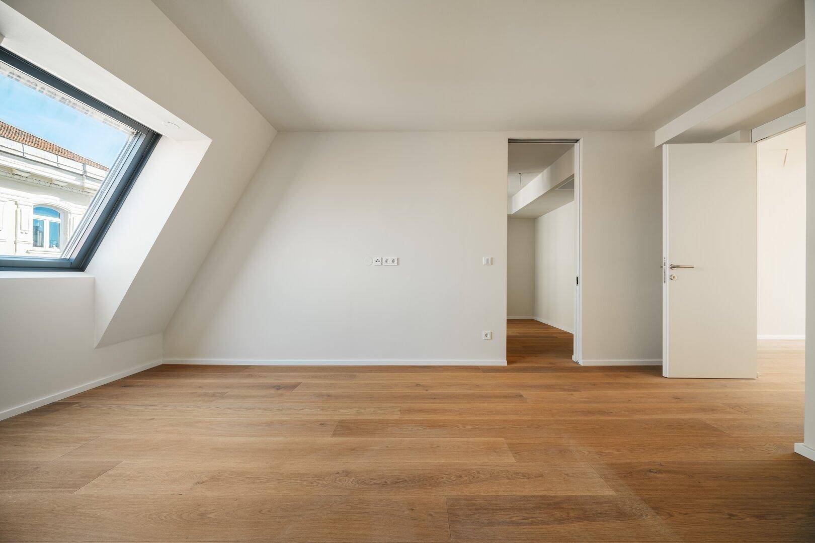 Dachgeschosszimmer mit Holzboden und schrägem Dachfenster, bietet eine gemütliche Atmosphäre.