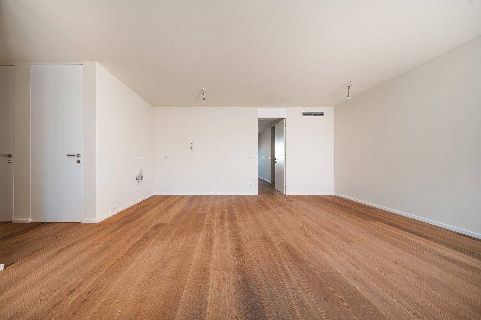 Leeres Zimmer mit Holzboden und weißen Wänden, bietet viel Potenzial für individuelle Einrichtung.