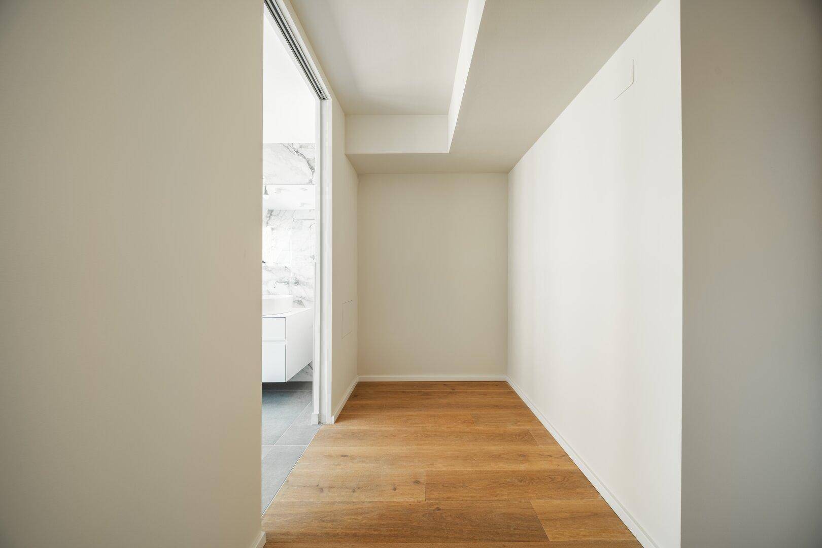 Heller Flur mit Holzboden, der zu einem modernen Badezimmer führt.