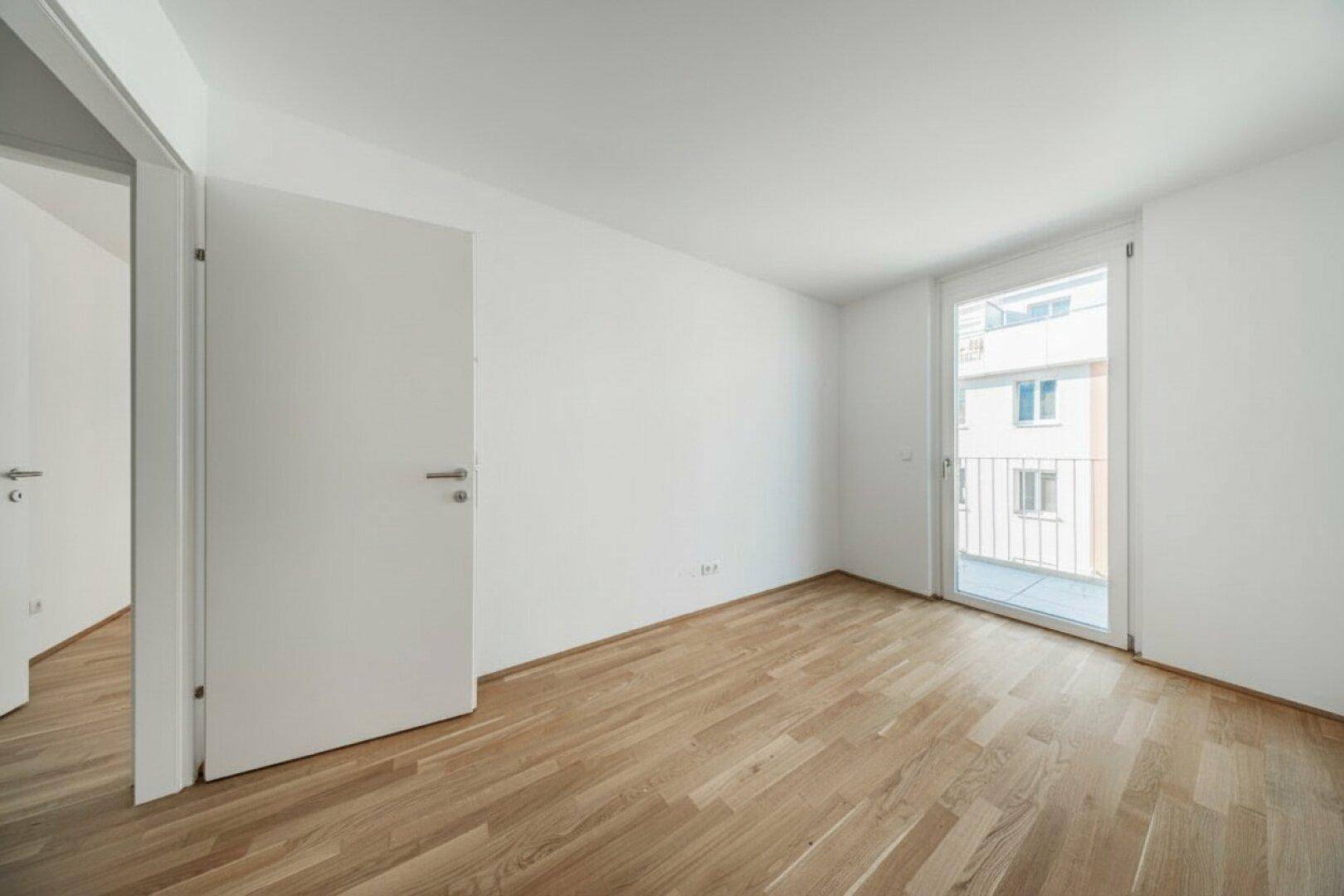 Helles, leeres Schlafzimmer mit Holzboden und Zugang zu einem französischen Balkon.