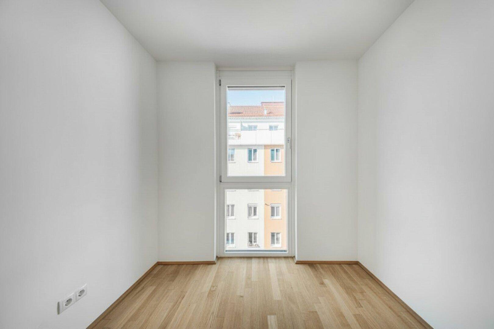Helles, leeres Zimmer mit Parkettboden und hohem Fenster, geeignet als Schlaf- oder Kinderzimmer.