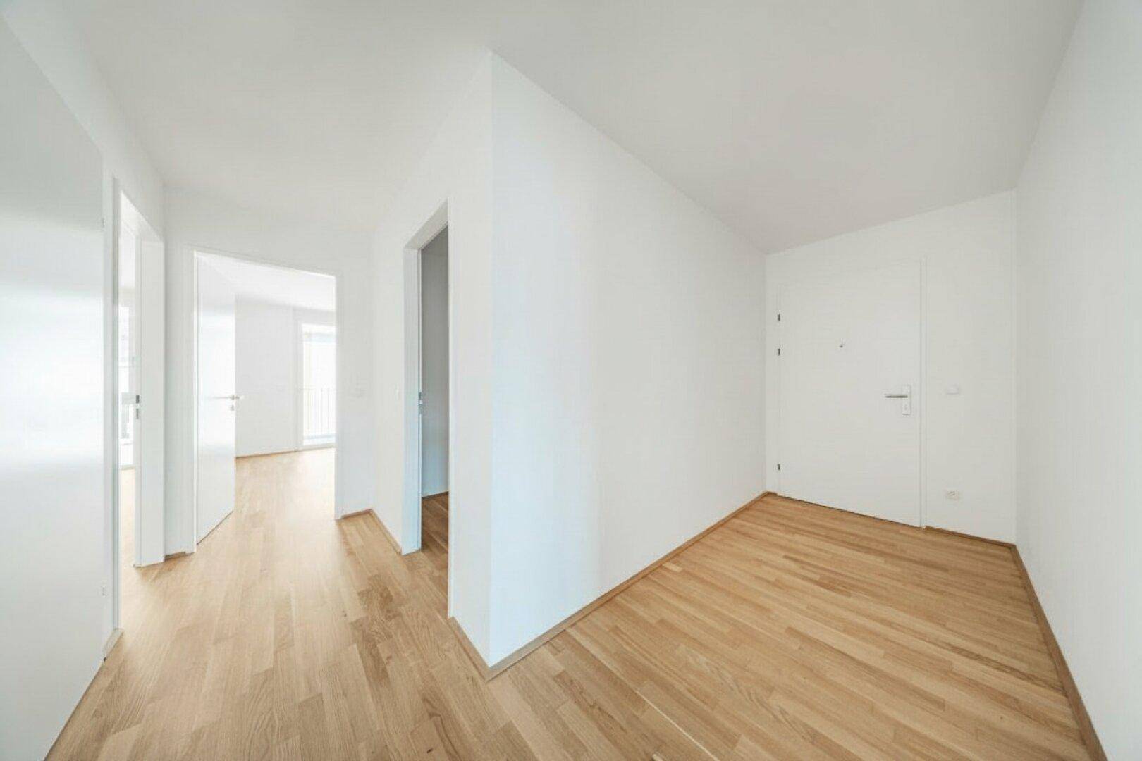 Heller Eingangsbereich mit Holzboden und weißer Eingangstür, führt in den Wohnbereich.
