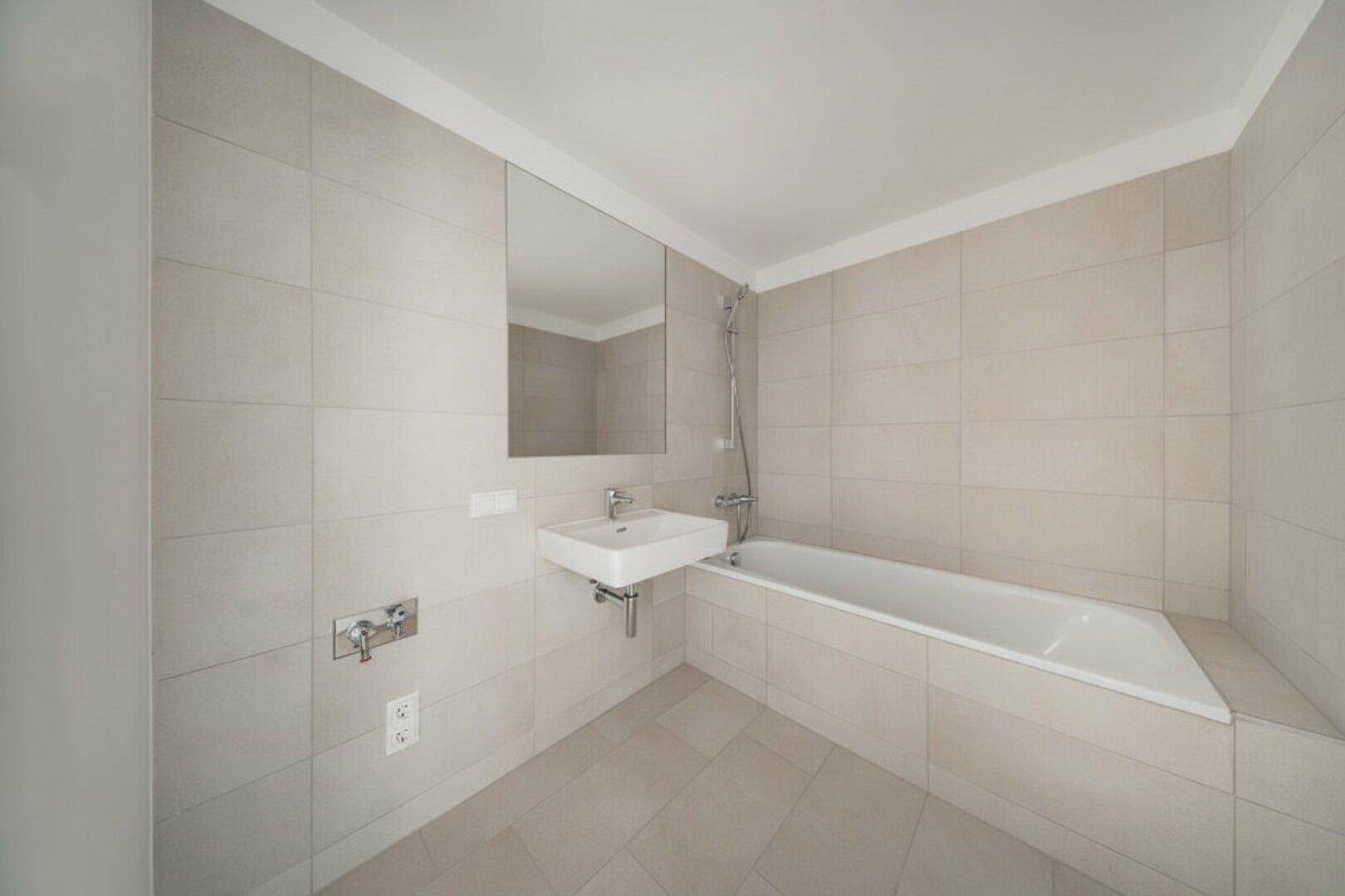 Modernes Badezimmer mit hellen Fliesen, Badewanne und Waschbecken, in neutralen Farben gehalten.