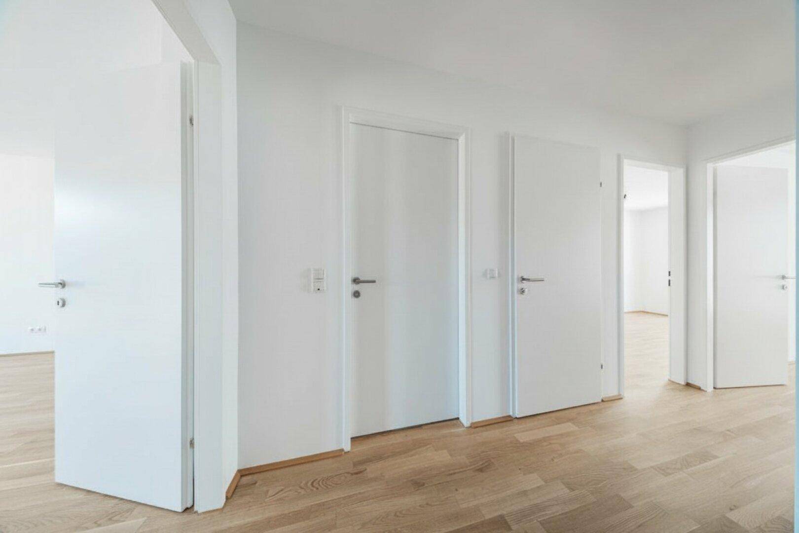 Heller Flur mit Holzboden und mehreren weißen Türen, der zu verschiedenen Räumen führt.