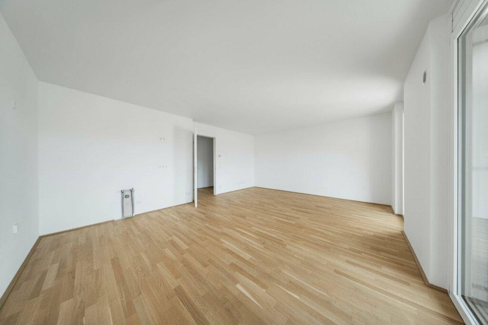 Leerer Raum mit Parkettboden und sichtbaren Anschlüssen an der Wand, bereit für die Einrichtung.