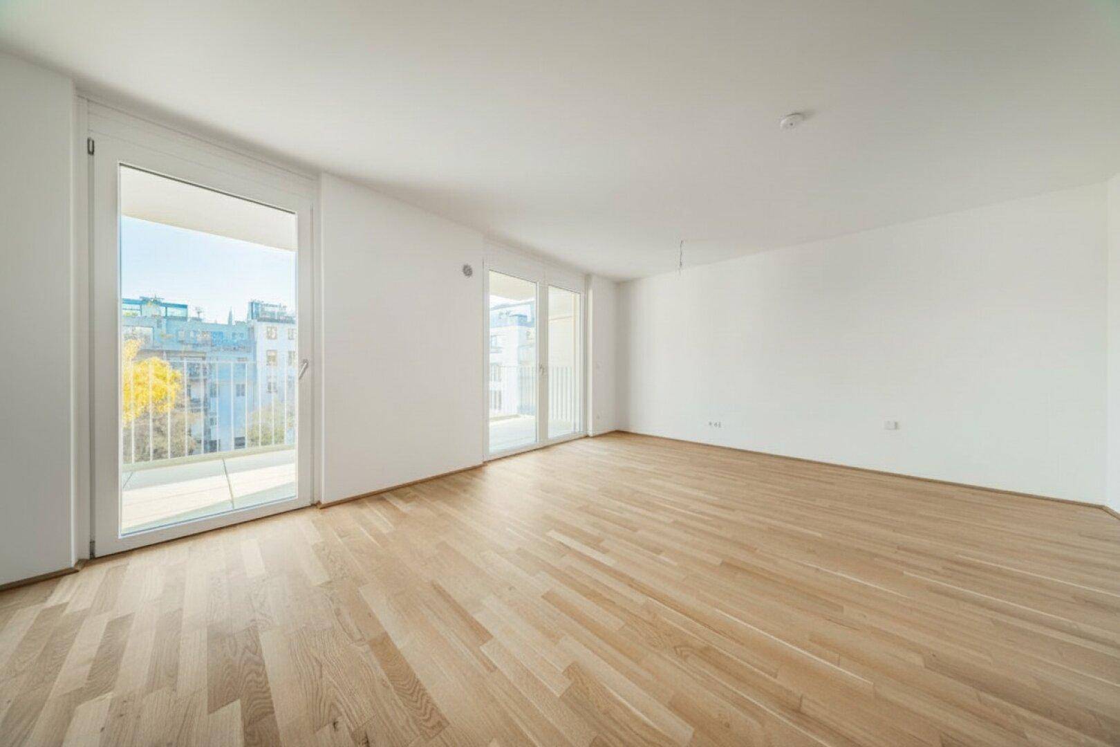 Großes, helles Wohnzimmer mit Parkettboden und mehreren Zugängen zu den Balkonen.