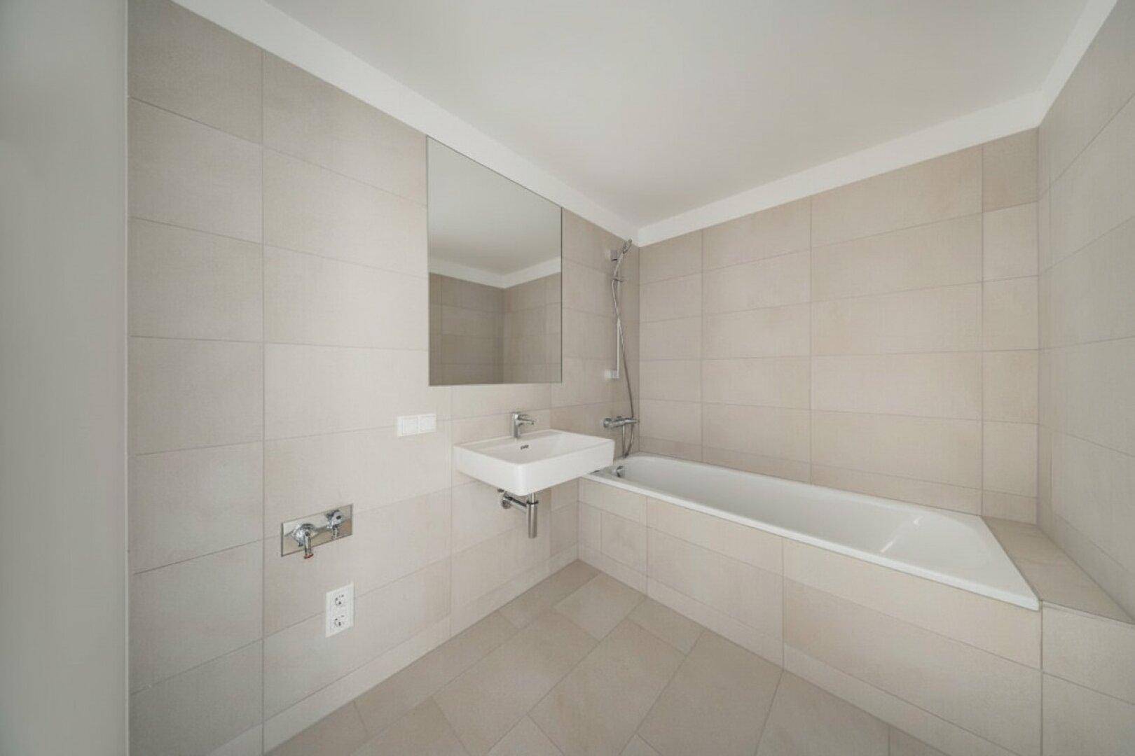 Modernes Badezimmer mit hellen Fliesen, Badewanne und einem schwebenden Waschbecken mit Spiegel.