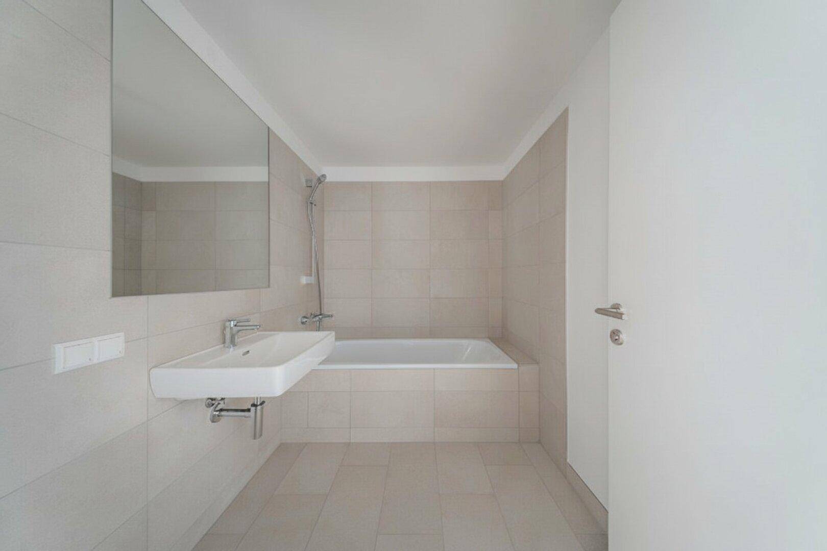 Helles Badezimmer mit beigefarbenen Fliesen, Badewanne und einem modernen Waschbecken mit Armatur.