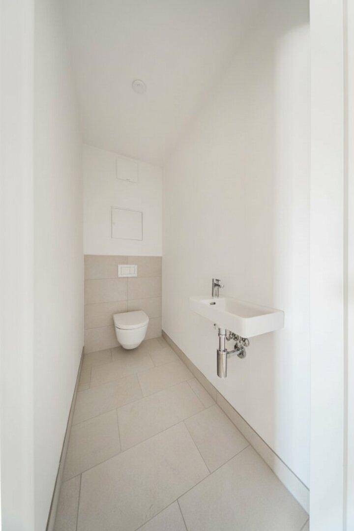 Modernes Gäste-WC mit wandhängender Toilette und kleinem Waschbecken in hellen Fliesen.