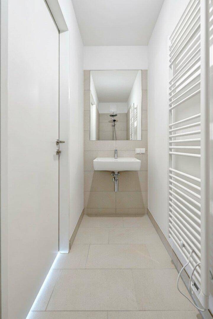 Kleines Badezimmer mit beigefarbenen Fliesen, Einzelwaschbecken, Spiegel und beheiztem Handtuchhalter.