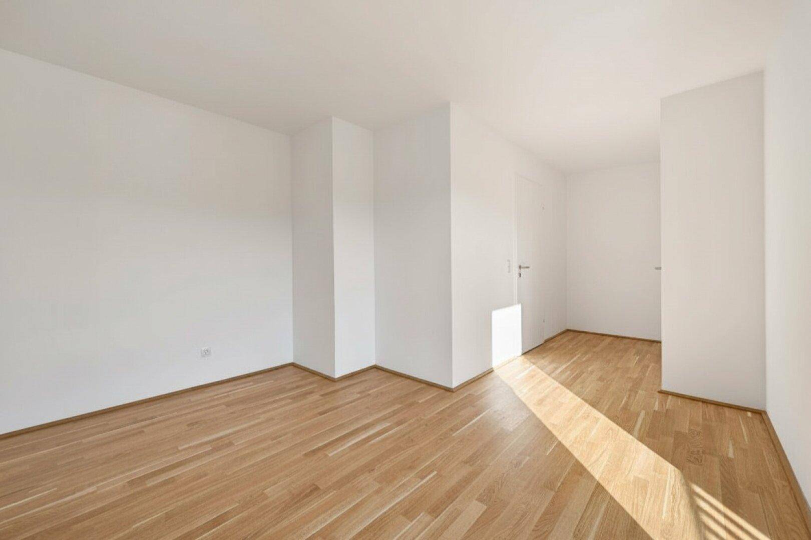 Lichtdurchfluteter Raum mit hellem Parkettboden und weißen Wänden, ideal für Wohn- oder Schlafzimmer.