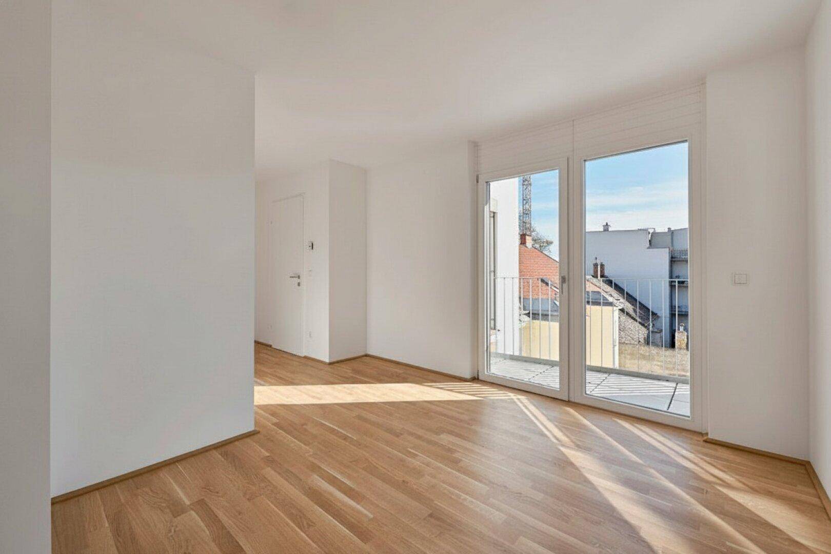 Heller Wohnraum mit Parkettboden und großem Fenster, das Zugang zu einem Balkon bietet.
