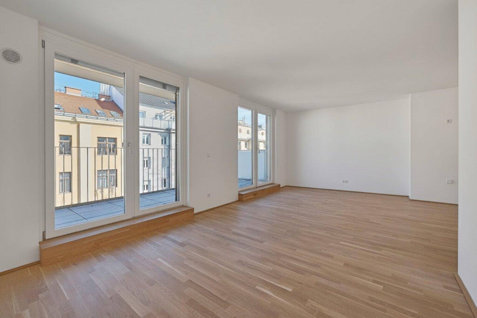 Geräumiger, heller Raum mit Parkettboden und zwei Balkonzugängen, bietet viel Tageslicht.