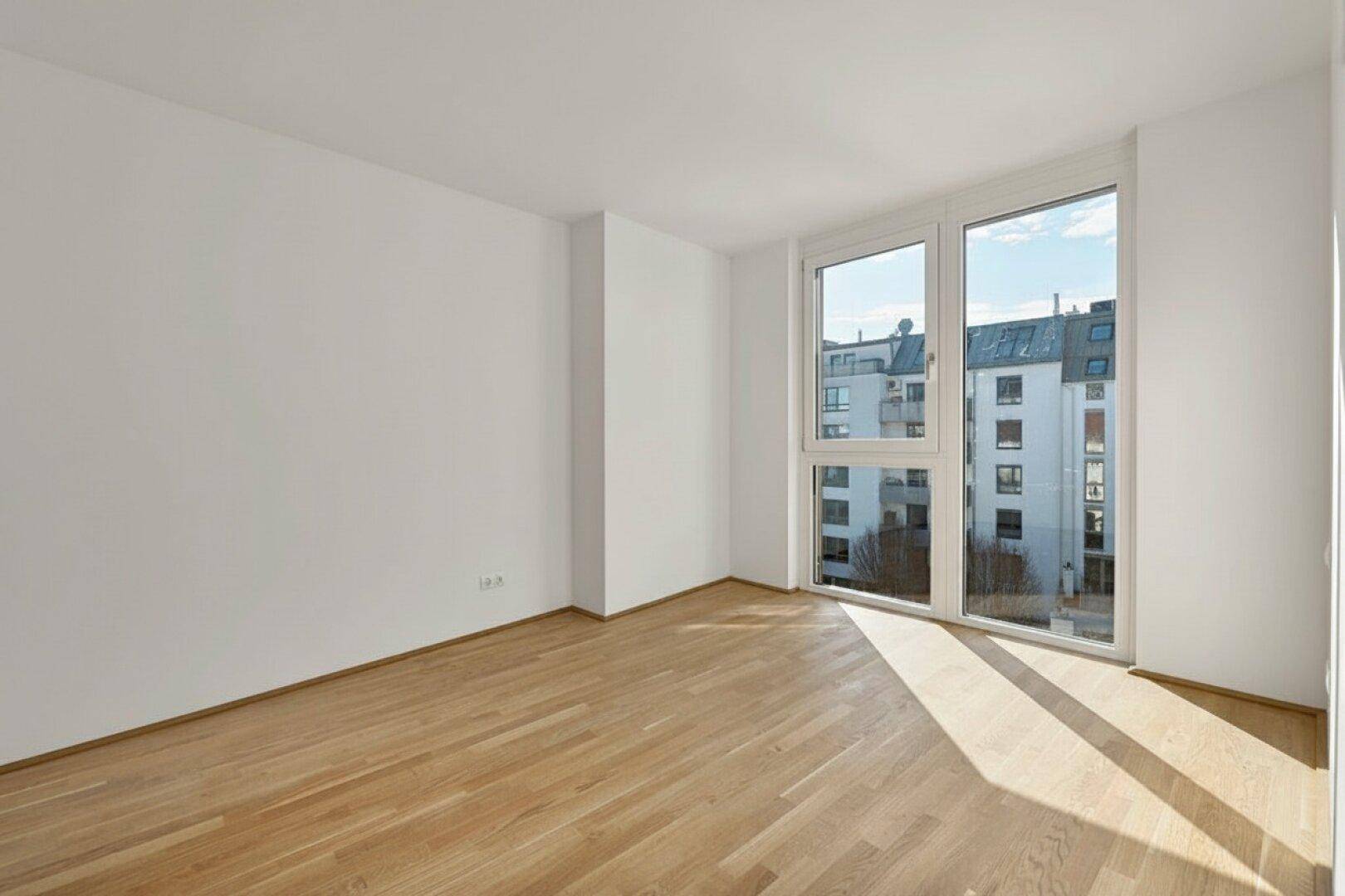 Leerer Raum mit großen Fenstern und Parkettboden, bietet viel natürliches Licht und Stadtblick.