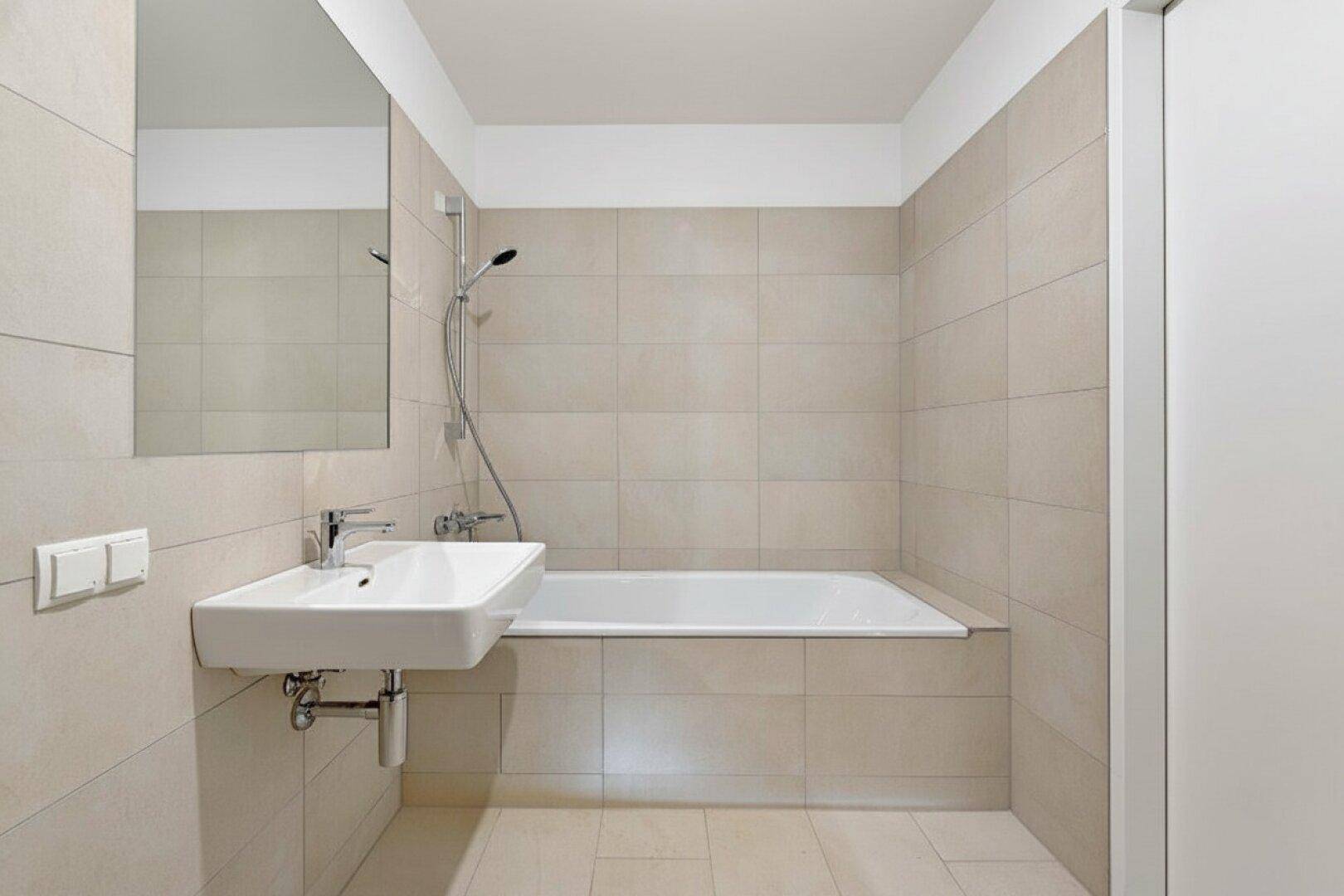 Helles Badezimmer mit Badewanne, Waschbecken und beigefarbenen Wand- und Bodenfliesen.
