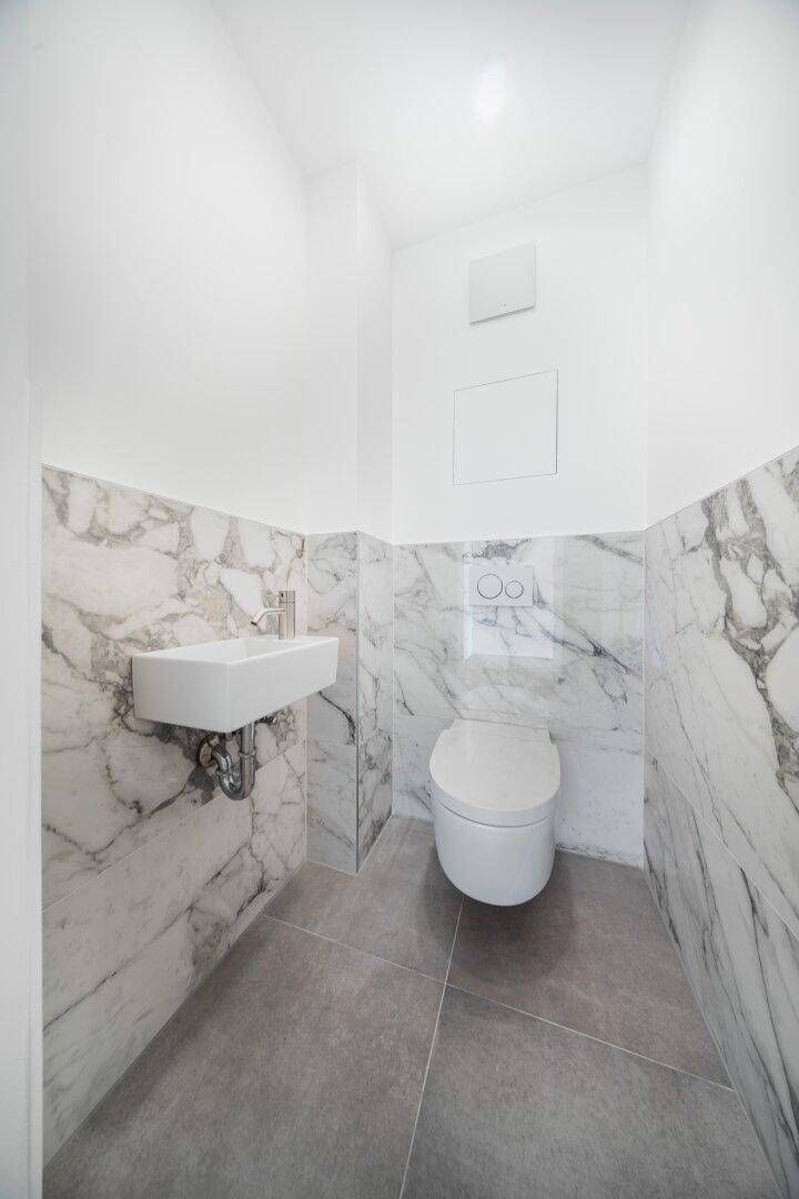 Elegantes Gäste-WC mit Marmorfliesen, wandhängender Toilette und kleinem Waschbecken.