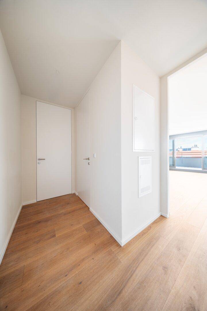 Heller Flur mit Holzboden und weiß gestrichenen Wänden, führt zu anderen Räumen.