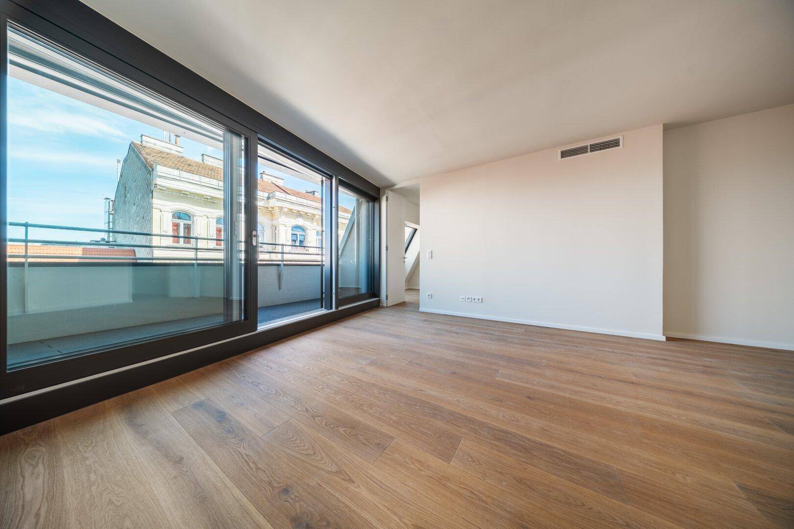 Helles, leeres Zimmer mit großen Schiebetüren zum Balkon und Holzboden.