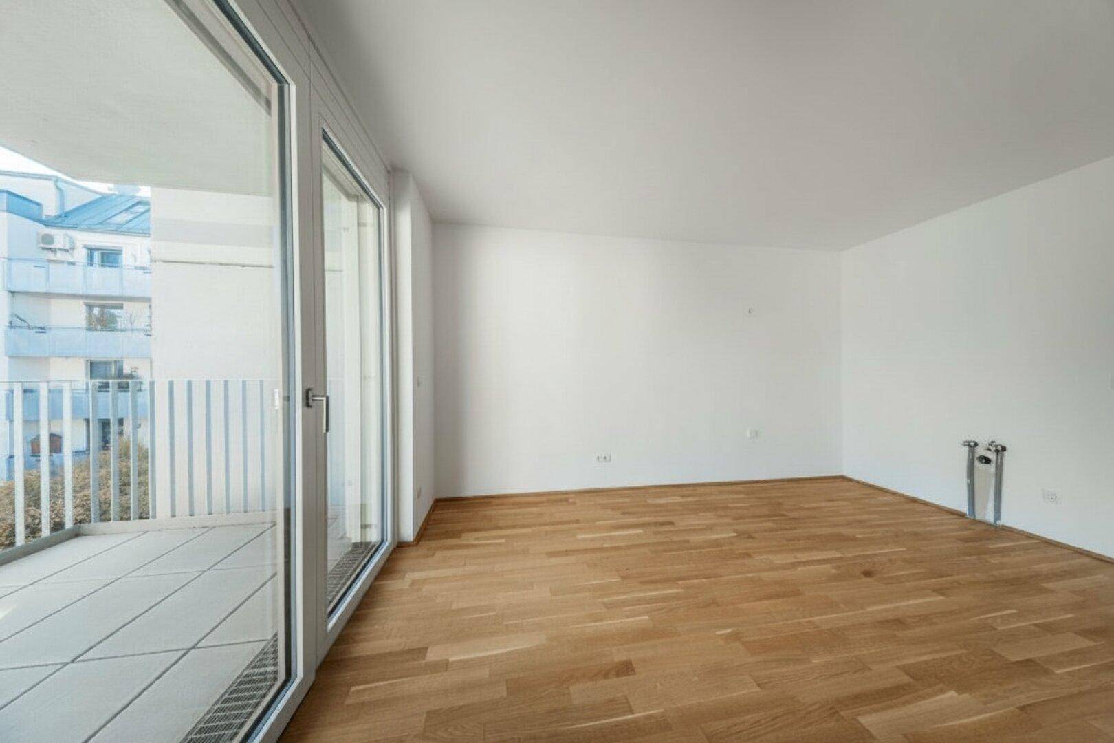 Geräumiges, helles Zimmer mit Holzboden und großem Fenster mit Blick auf die Umgebung.