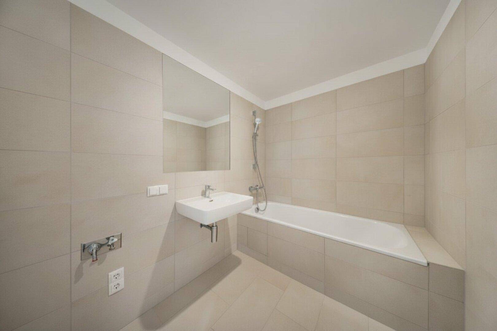 Modernes Badezimmer mit beigefarbenen Fliesen, Badewanne und einem einzelnen Waschbecken.