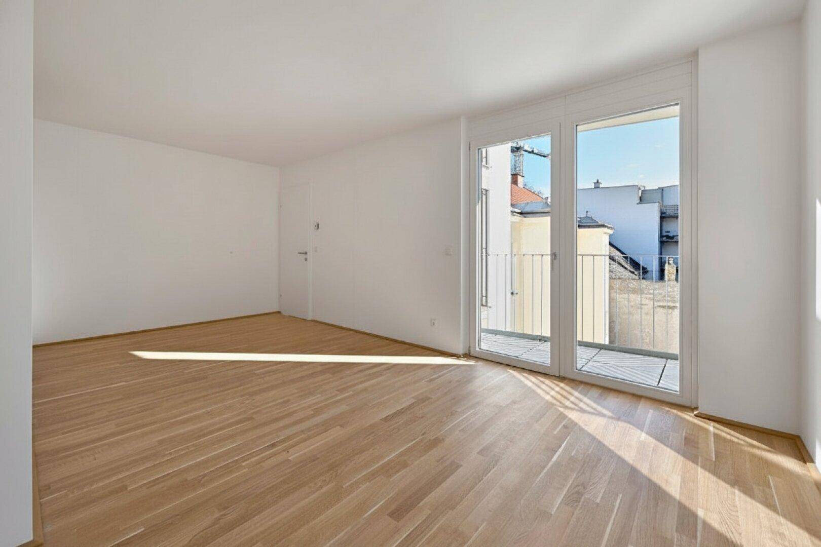 Leerer Raum mit Holzboden und Zugang zu einem französischen Balkon, hell und offen.