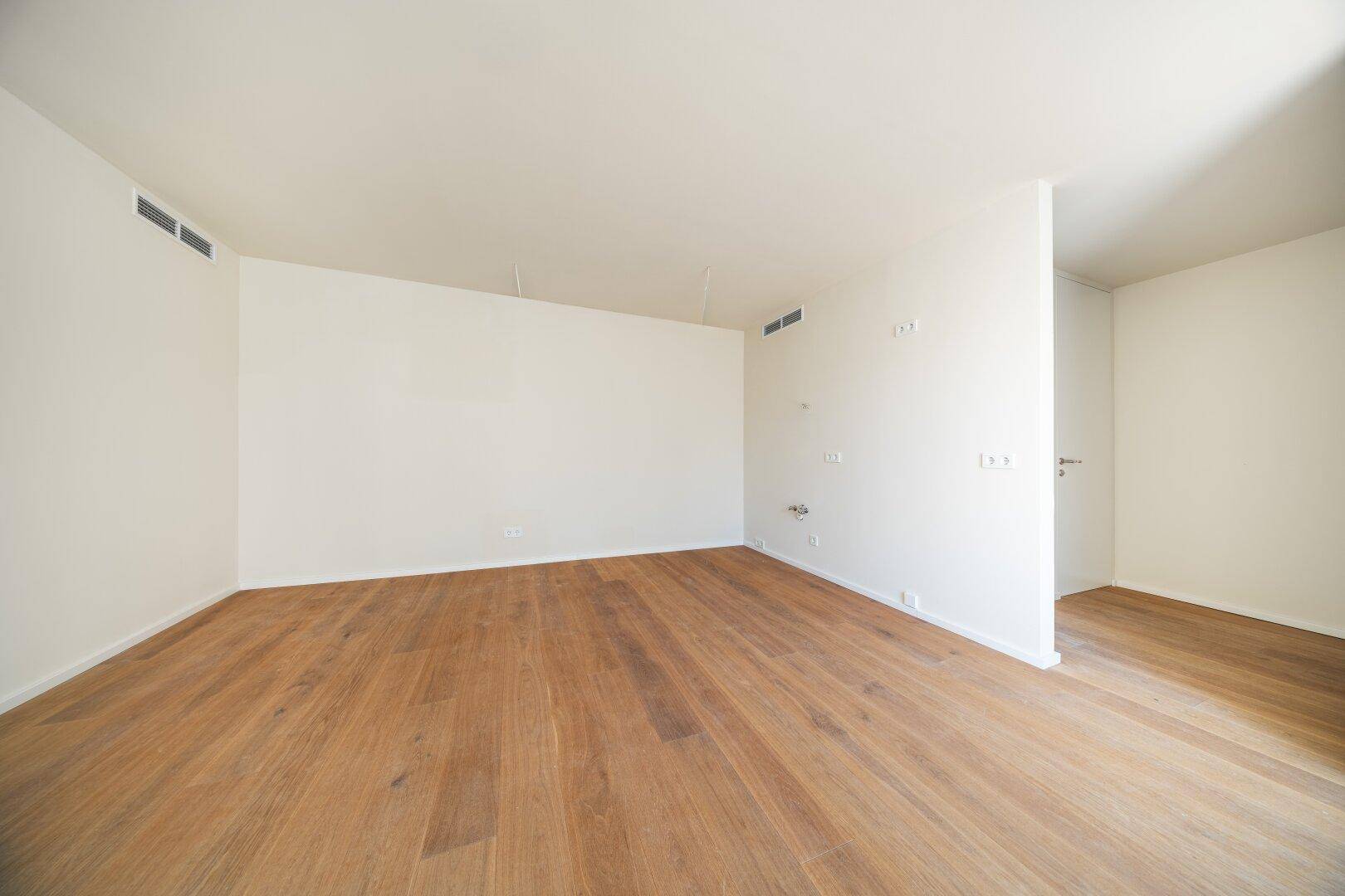 Leerer, heller Raum mit Holzboden und weißen Wänden, bereit zur individuellen Gestaltung.