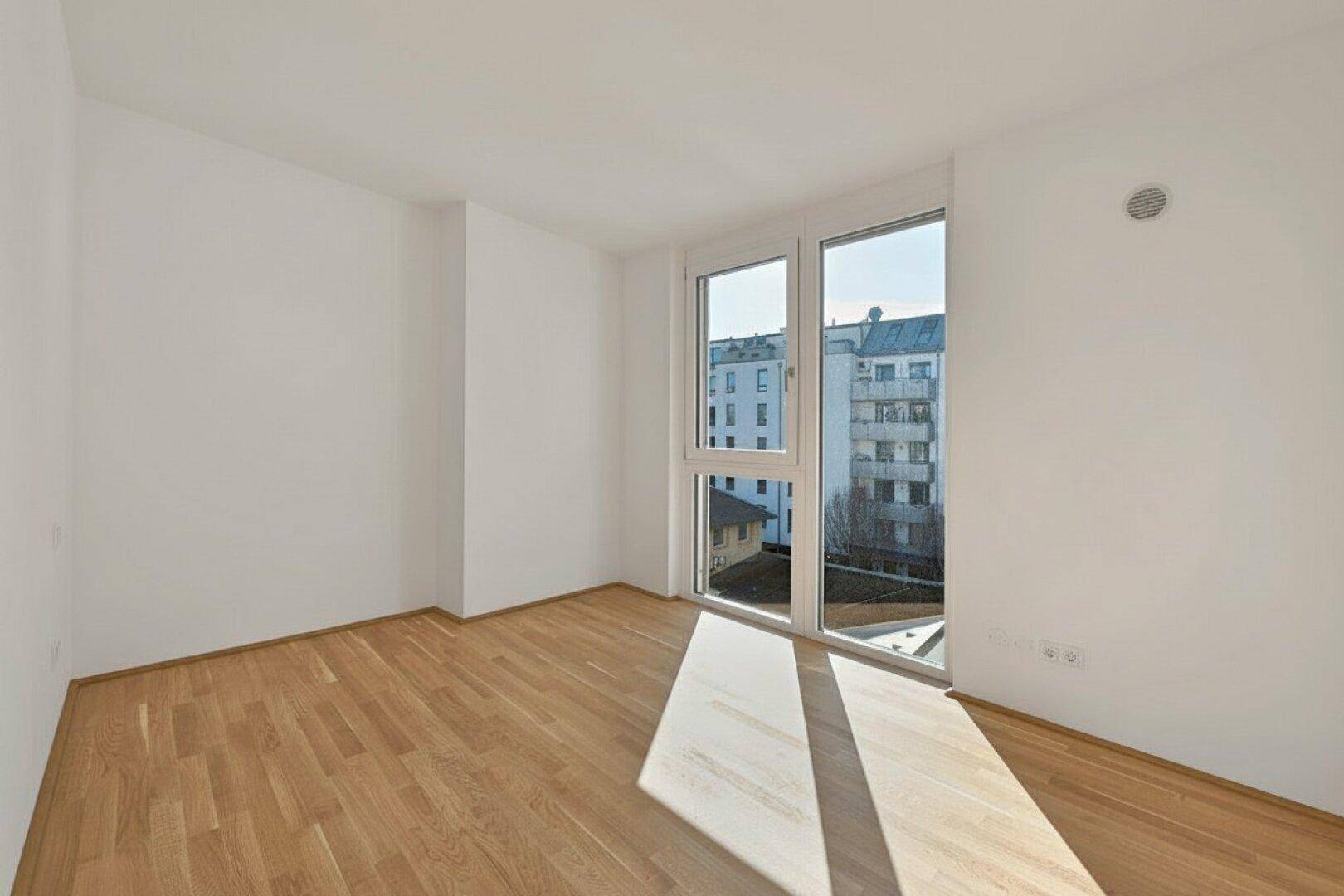 Heller, leerer Raum mit Holzboden und Fenster, das einen Blick auf die Stadt bietet.