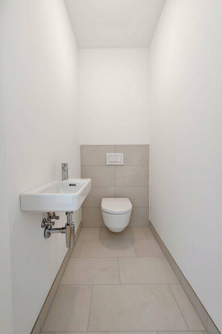 Modernes Gäste-WC mit Wand-WC und kleinem Waschbecken, in hellen Fliesen gehalten.