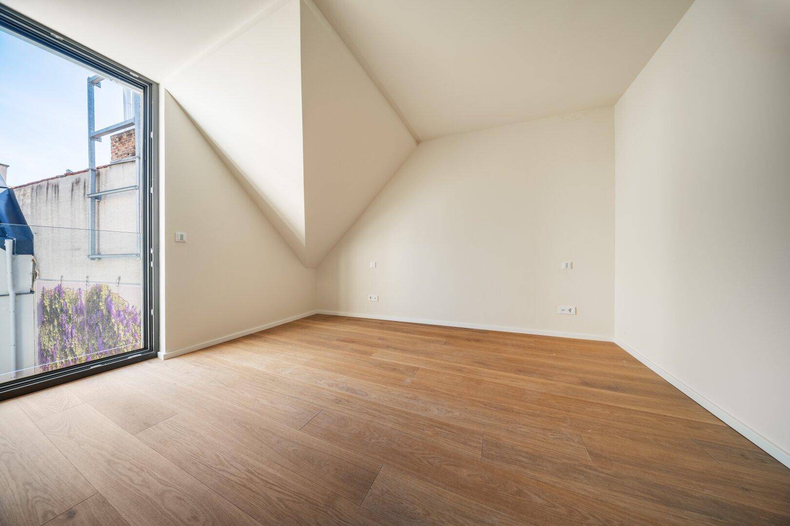 Helles Schlafzimmer im Dachgeschoss mit Holzboden und großem Fenster mit Blick nach draußen.