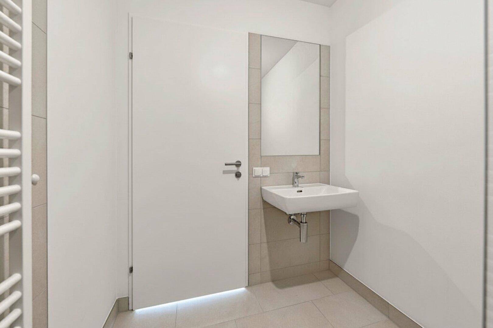 Modernes Badezimmer mit Waschbecken, Spiegel und beheiztem Handtuchhalter, in hellen Tönen.