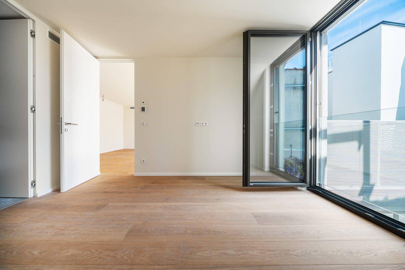 Geräumiges, helles Zimmer mit Holzboden und Zugang zu einem Balkon oder einer Terrasse.