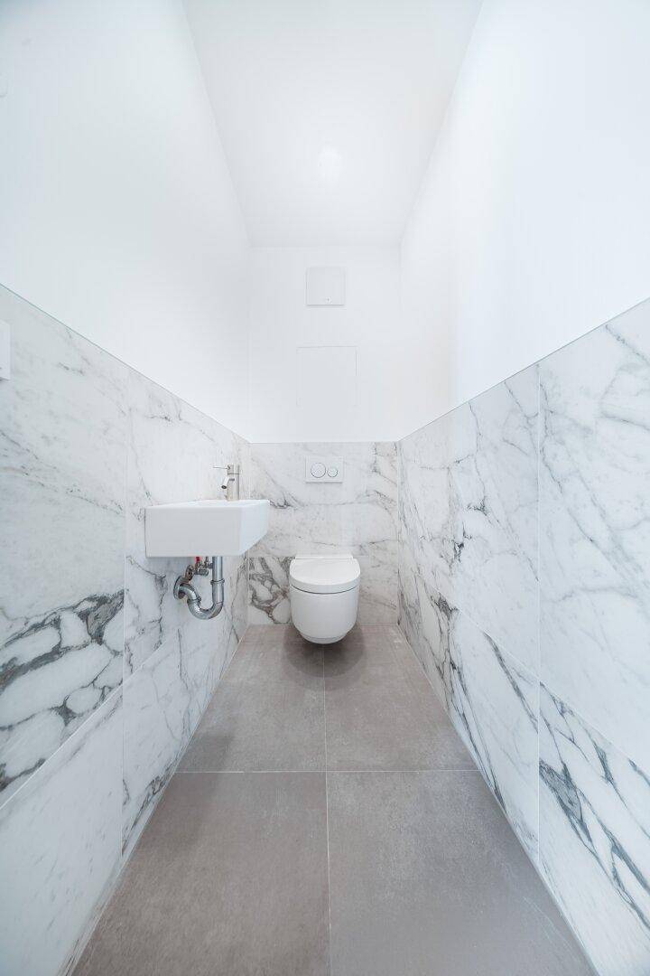 Modernes Gäste-WC mit Marmorfliesen, wandhängender Toilette und kleinem Waschbecken.