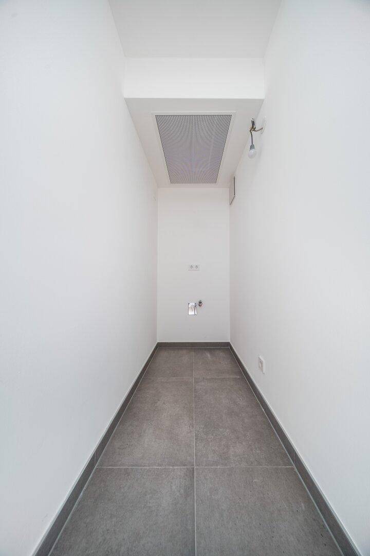 Schmaler Hauswirtschaftsraum mit Fliesenboden und weiß gestrichenen Wänden.