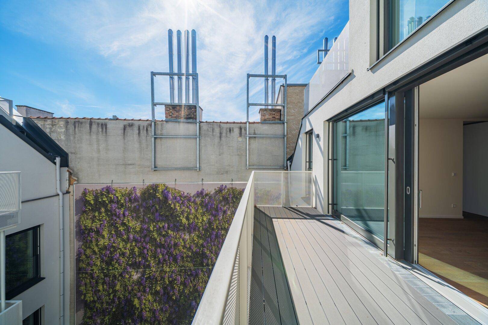 Moderner Balkon mit Holzboden und Blick auf eine begrünte Wand und Dächer.