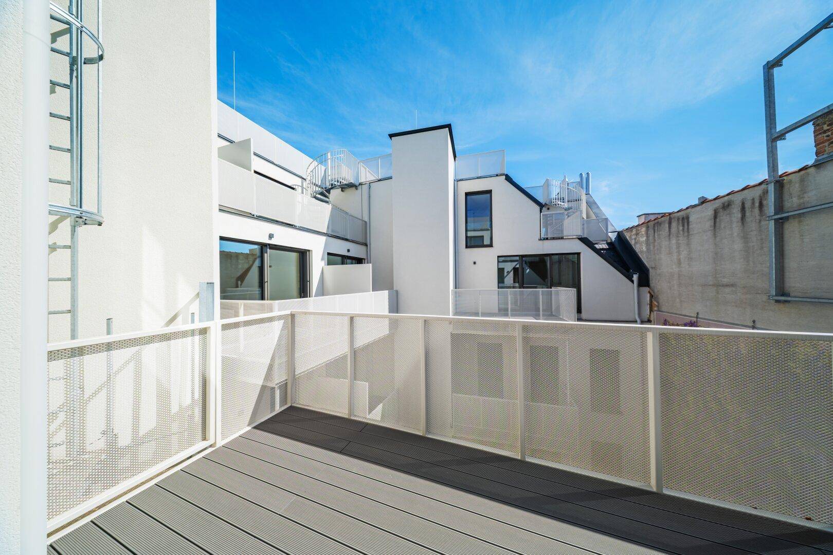 Heller Balkon mit Gittergeländer und Blick auf die moderne Architektur des Innenhofs.