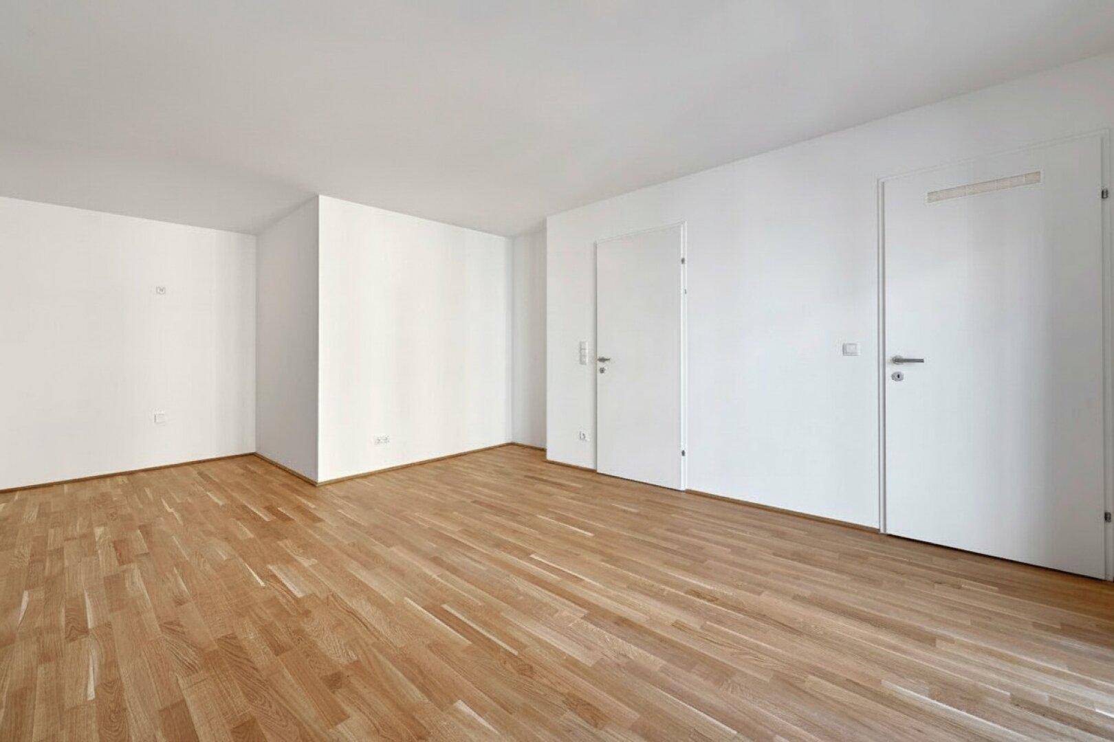 Geräumiges, helles Zimmer mit Holzboden und weißen Wänden, ideal für flexible Einrichtung.