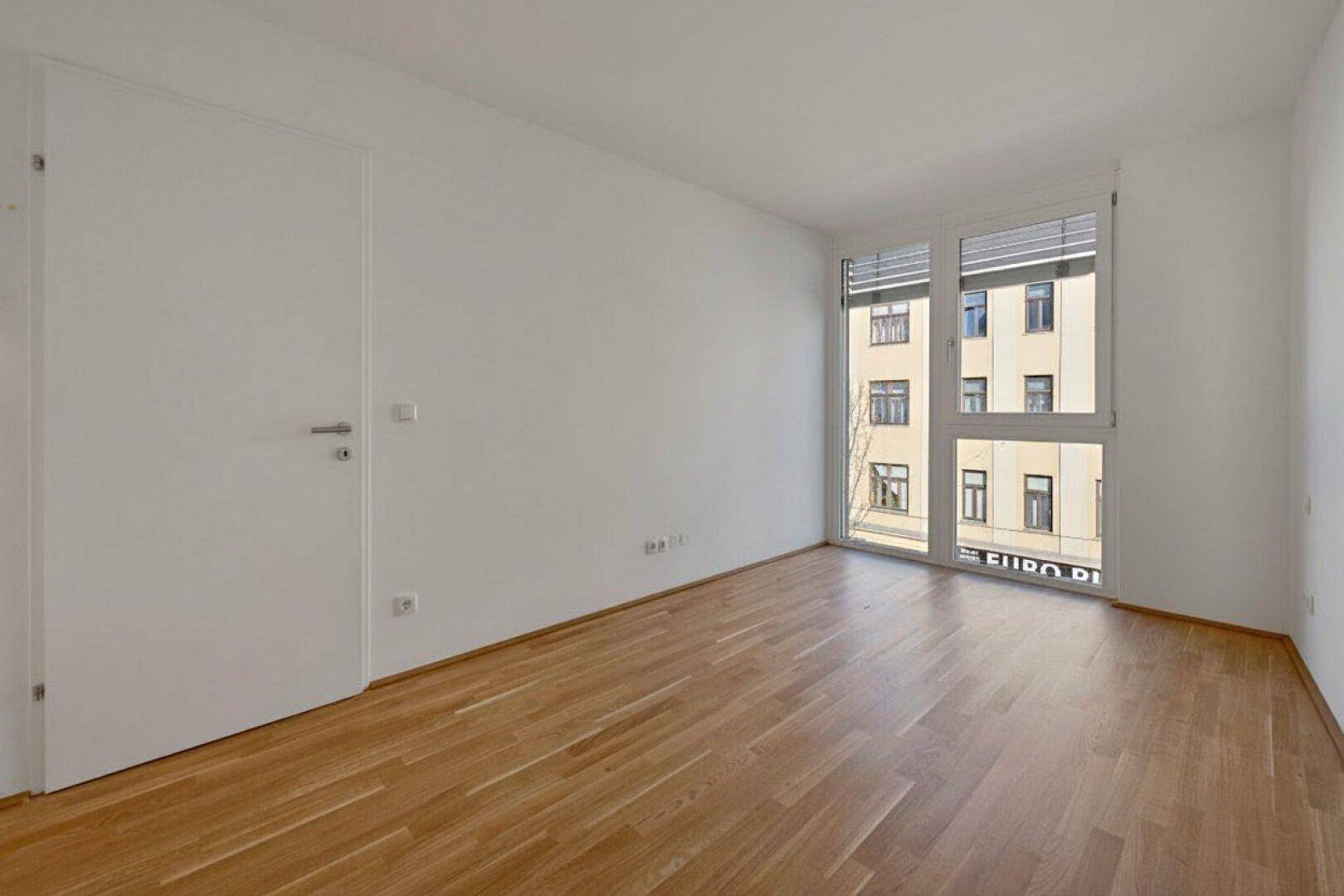 Leerer Raum mit großen Fenstern und Holzboden, ideal für ein Schlafzimmer oder Büro.