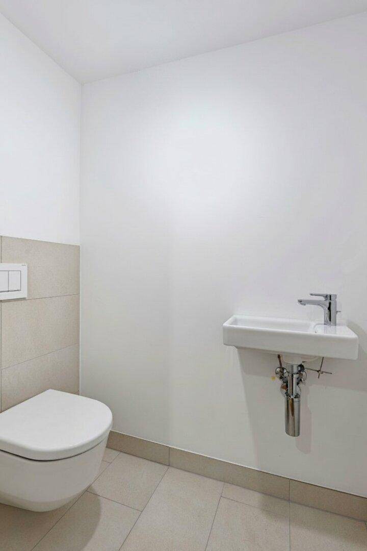 Modernes Gäste-WC mit Wand-WC, kleinem Waschbecken und hellen Fliesen.