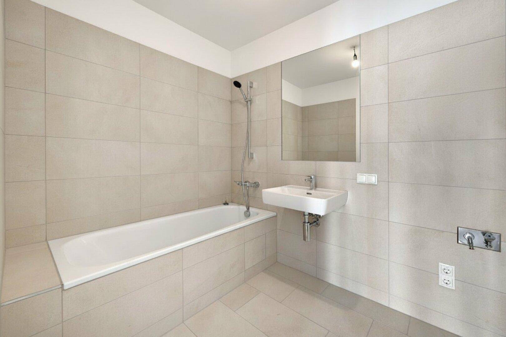 Modernes Badezimmer mit Badewanne, Waschbecken und großen, hellen Wand- und Bodenfliesen.