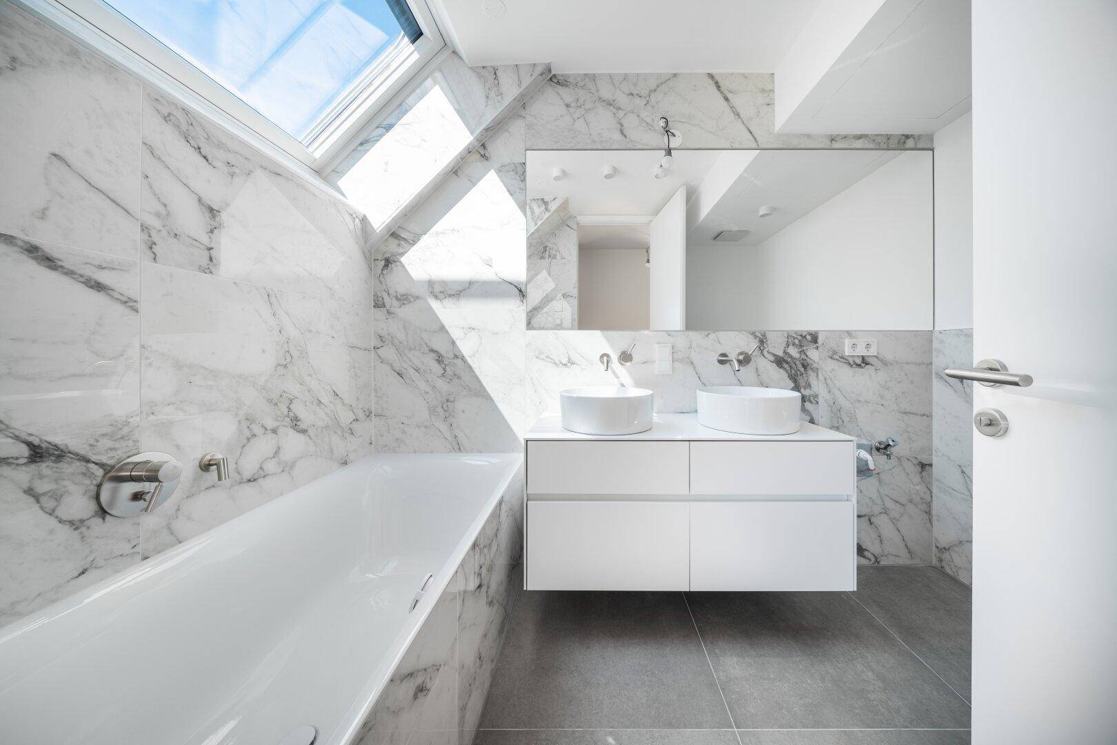 Modernes Badezimmer mit Marmorfliesen, Doppelwaschbecken, Badewanne und Dachfenster für viel Licht.