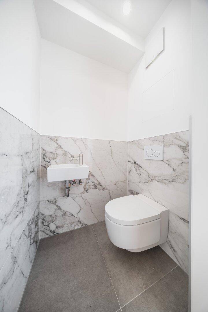 Elegantes Gäste-WC mit Marmorfliesen, wandhängendem WC und kleinem Waschbecken.