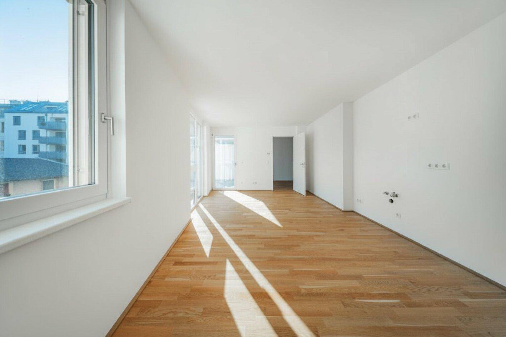 Lichtdurchfluteter Raum mit Holzparkett und großen Fenstern, die einen Blick nach draußen bieten.