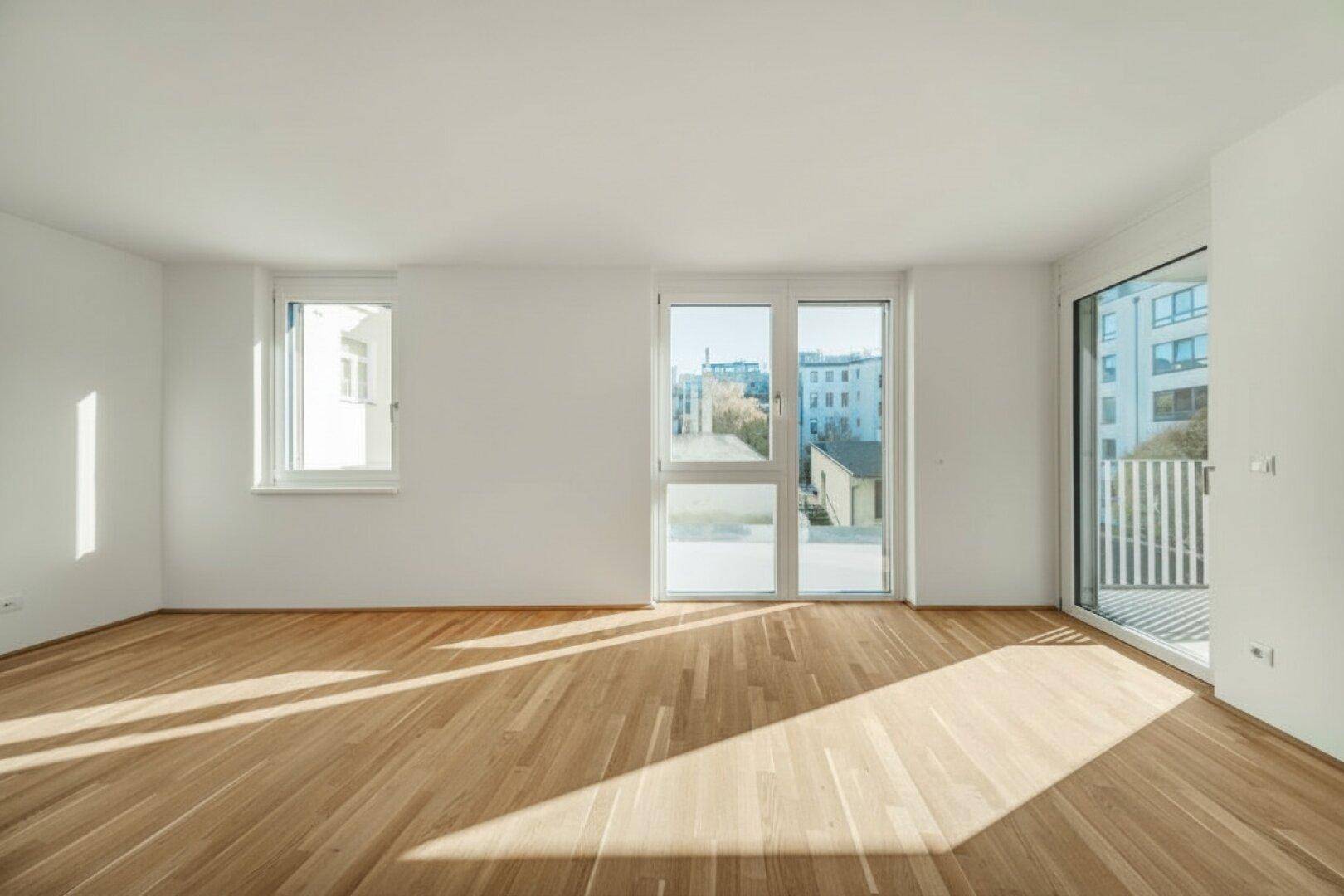 Geräumiges Zimmer mit Parkettboden und Zugang zu einem Balkon, der viel Sonnenlicht hereinlässt.
