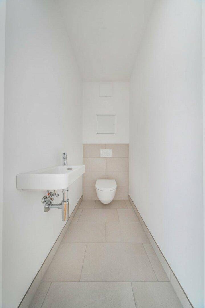 Modernes Gäste-WC mit wandhängender Toilette und kleinem Waschbecken, in hellen Fliesen gehalten.