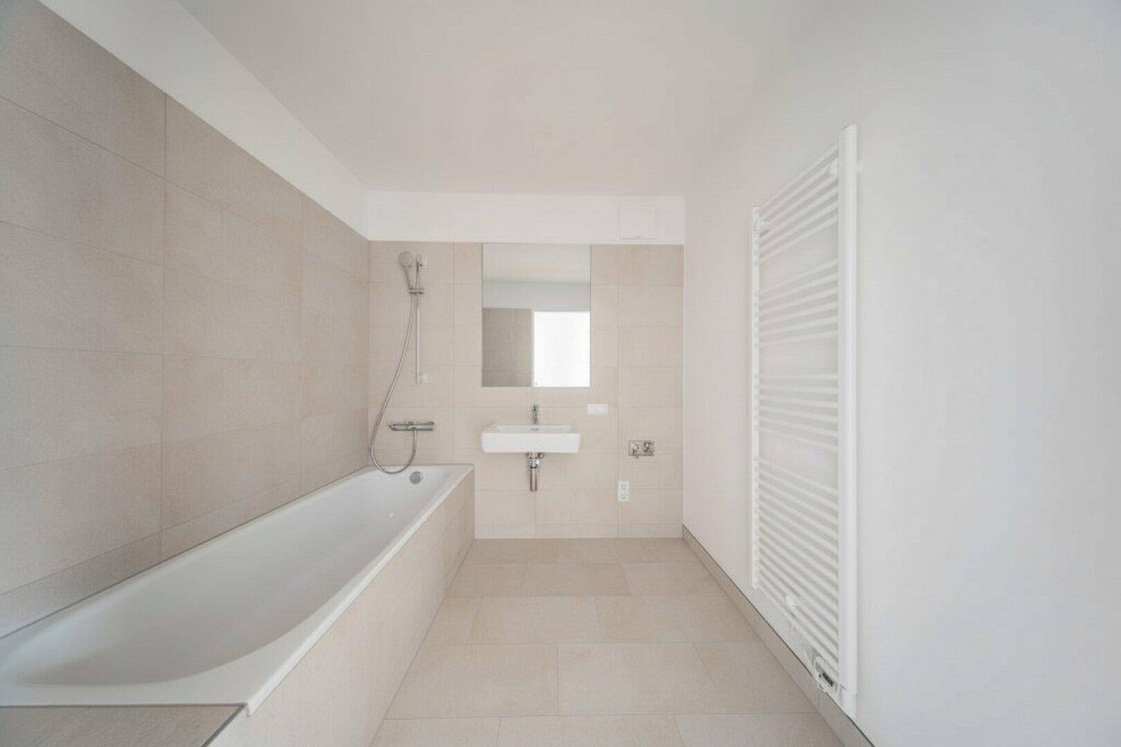 Modernes Badezimmer mit Badewanne, Waschbecken und beheiztem Handtuchhalter, in hellen Beigetönen gefliest.
