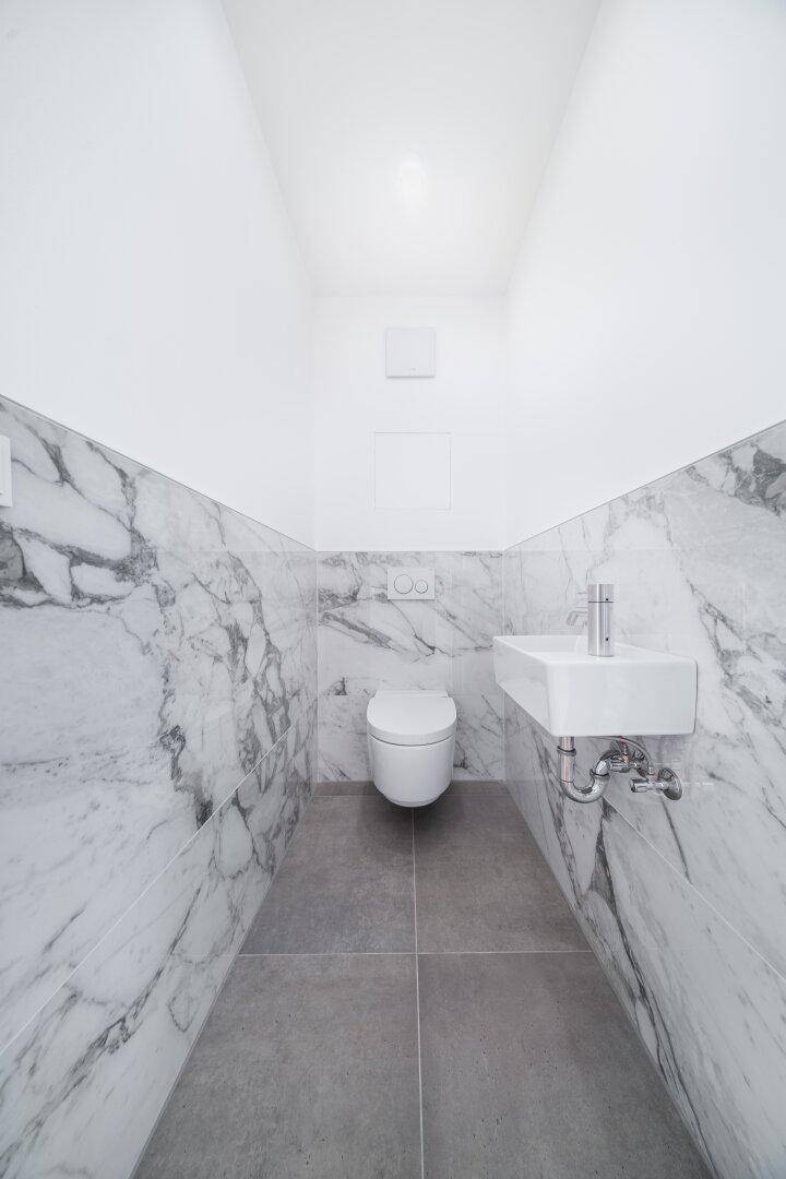 Modernes Gäste-WC mit Marmorfliesen und wandhängendem WC sowie kleinem Waschbecken.