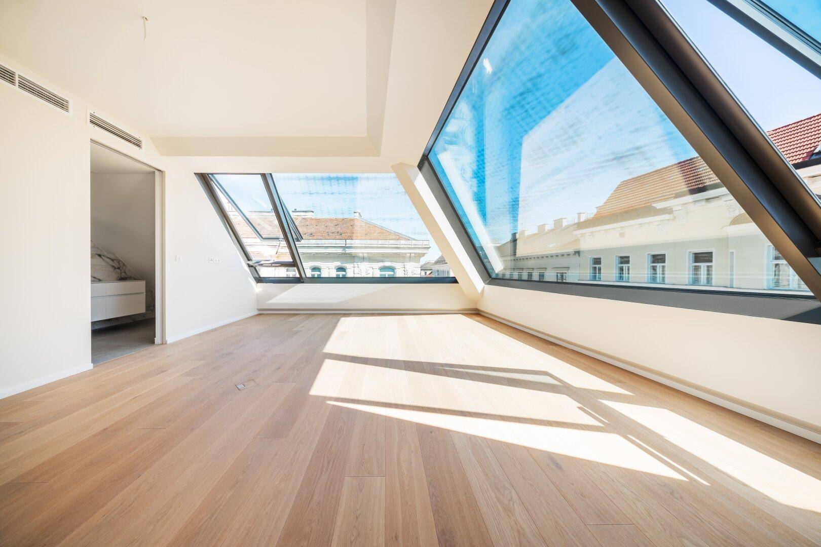 Geräumiger, heller Raum mit schrägen Fenstern und Holzboden, ideal für individuelle Gestaltung.