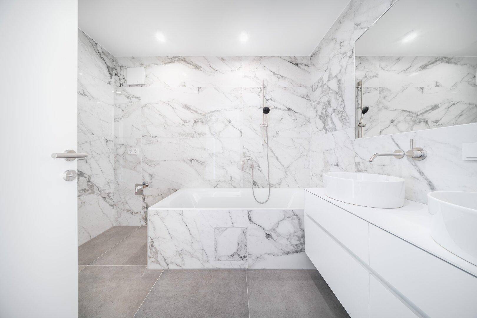 Modernes Badezimmer mit Marmorfliesen, Badewanne und Doppelwaschbecken in Weiß.